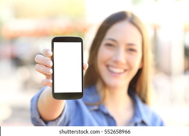 Front View Of A Happy Girl Showing A Blank Smart Phone Display And Looking To The Camera In The Street