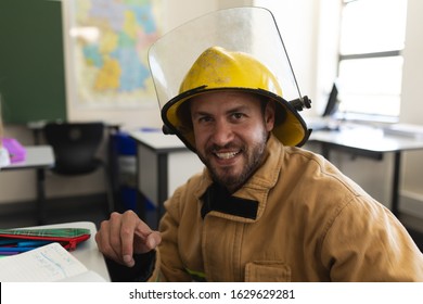 Front View Of Happy Male Caucasian Firefighter With Helmet Looking At Camera In Classroom Of Elementary School