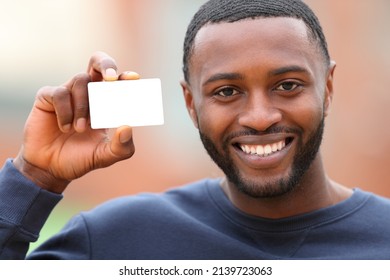 Front view of a happy man with black skin showing blank credit card in the street