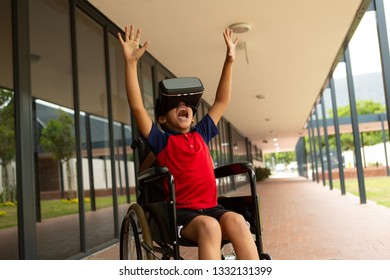 Front view of happy mixed-race disabled schoolboy using virtual reality headset with his hands in the air in corridor at elementary school - Powered by Shutterstock