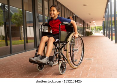 Front view of happy mixed-race disabled schoolboy sitting on wheelchair in corridor at elementary school - Powered by Shutterstock