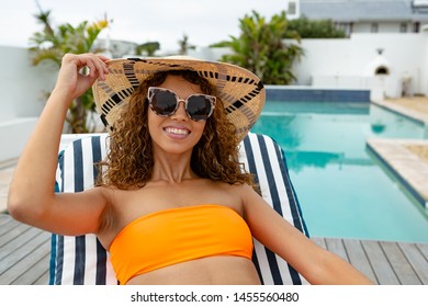 Front View Of Happy Mixed-race Woman In Bikini Relaxing On A Sun Lounger Near Swimming Pool At The Backyard Of Home. Summer Fun At Home By The Swimming Pool