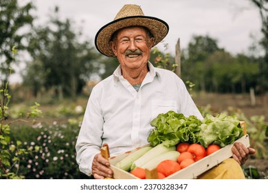 Front view of a happy old man sitting in his garden holding a crate with organic vegetables. - Powered by Shutterstock