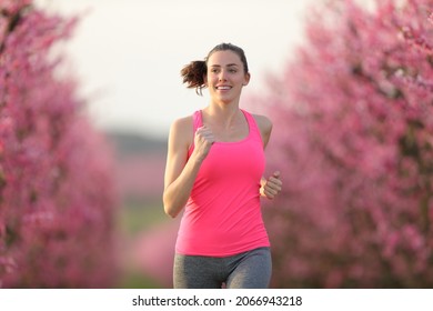 Front view of happy runner running towards camera in a pink flowered field - Powered by Shutterstock