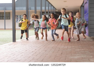 Front view of happy school kids running in corridor at school - Shutterstock ID 1352249729