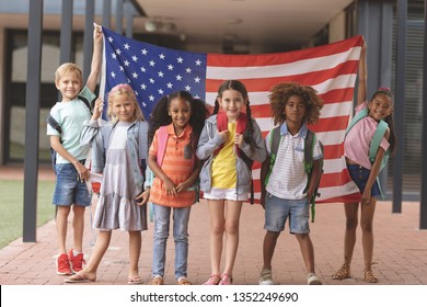 Front view of happy school students standing in outside corridor at school while holding american flag  - Powered by Shutterstock