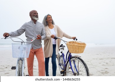 Front view of happy senior African-American couple standing with bicycles on the beach on cloudy day. Authentic Senior Retired Life Concept - Powered by Shutterstock