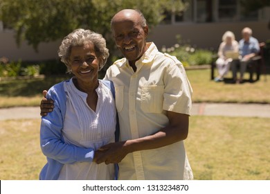Front view of happy senior couple holding hands and looking at camera in garden