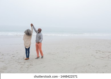 Front view of happy senior diverse couple dancing on the beach on cloudy day. Authentic Senior Retired Life Concept - Powered by Shutterstock