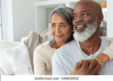 Front View Of Happy Senior Diverse Couple Sitting On White Couch In Beautiful Beach House. Authentic Senior Retired Life Concept