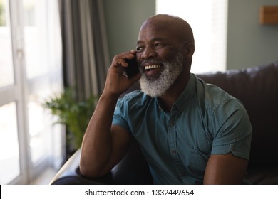 Front view of happy senior man talking on mobile phone in living room at home - Powered by Shutterstock