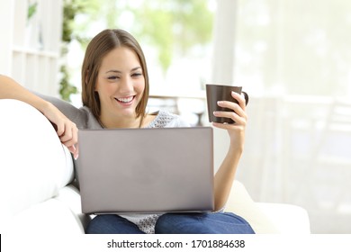 Frohes Beisammensein, das auf einem Laptop mit Kaffeetasse sitzend auf einem Sofa zu Hause liest