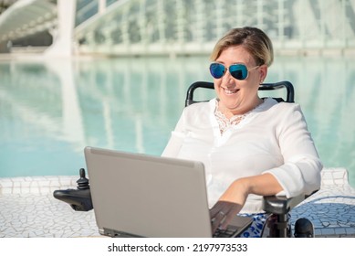 Front View Of A Happy Woman With Sunglasses In Wheelchair Using Laptop In Urban Outdoor City Scenario