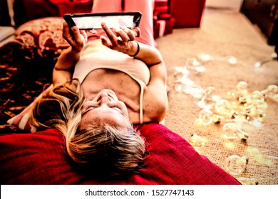 Front view of a happy young Caucasian woman lying on the floor and using a tablet in her sitting room at Christmas time