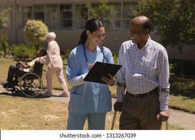 Front view of happy young female doctor discussing medical report with senior man on clipboard in garden - Powered by Shutterstock