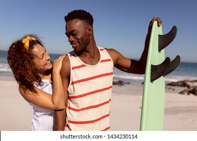 Front view of happy young Mixed-race couple with surfboard looking each other on beach in the sunshine