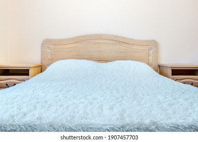 Front View Of Headboard Of Simple Cheap Wooden Bed With White Terry Cloth Blanket And Two Nightstands On Sides.