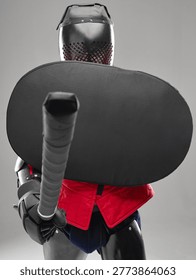Front view of HEMA fighter blocking with shield and extending padded sword in defensive stance.