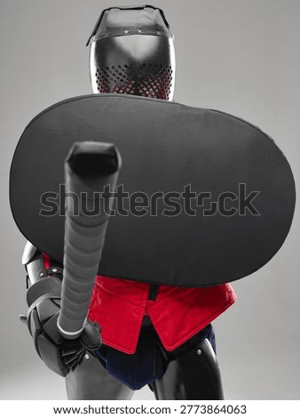 Front view of HEMA fighter blocking with shield and extending padded sword in defensive stance.