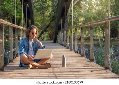 Front view of hipster young man working as digital nomad with laptop sorrounded by nature