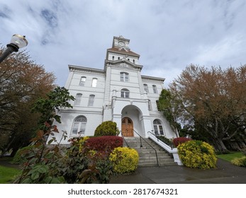 Front view of a historic Courthouse, featuring a detailed clock tower, grand stairs, landscaped lawns and colorful spring trees beneath a bright sky.