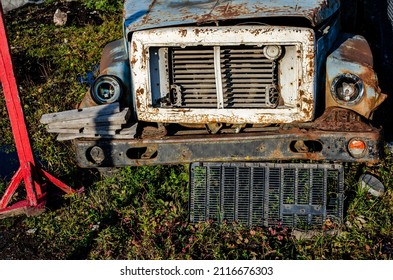 Front View Of The Hood Grille And Bumper Of A Rusty Blue Truck On A Parking Lot Of Broken Machinery