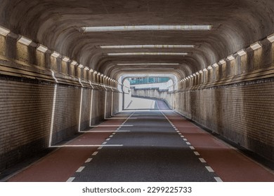 Front view of interior of an empty vehicular tunnel with cycle lanes with a curve in background, brick walls, concrete roof and openings where sunlight enters, Susteren, South Limburg, Netherlands