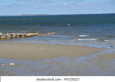 Front View Of A Isolated Lonely Beach With  Sand Floor Wet With The Movement Of The Deep Cold Water Ocean Shore Beach Sea Far Away Horizon Touching The Limitless Soft Blue Sky On The Background 