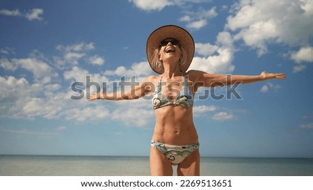 Front view of joyful happy mature senior woman turning with arms outstretched enjoying nature and freedom on beach at sunset sunrise.
