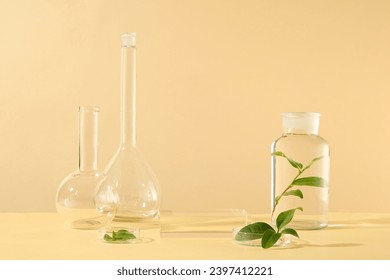 Front view of lab equipment decorated with green tea leaves on beige background. Laboratory concept with blank space on glass podium for cosmetic presentation. Advertising photo, space for design