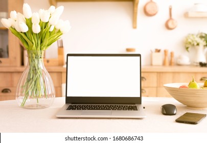 Front View Of Laptop With White Screen In A Kitchen With Soft And Warm Light.help In The Kitchen With New Technologies.isolation At Home By The Coronavirus Concept . Freelance. Flowers On The Table.