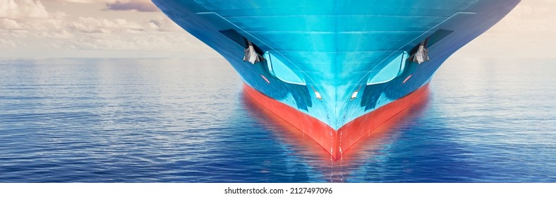Front view of large blue container cargo ship in the ocean. Performing cargo export and import operations with horizon line and beautiful sky.