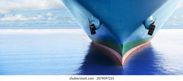 Front view of large blue merchant cargo ship in the middle of the ocean. Performing cargo export and import operations with horizon line and beautiful sky.