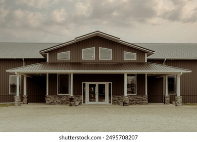 Front view of a large rustic building with a symmetrical design and a metal roof, set against a cloudy sky. Ideal for themes of architecture, rural living, and country style