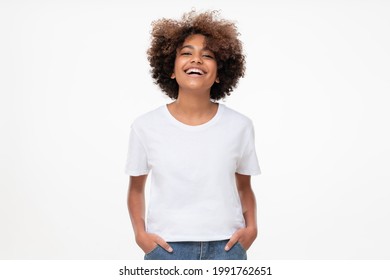 Front view of laughing african teen girl standing with hands in pockets, wearing white tshirt with copy space, isolated on gray background