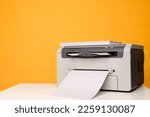 Front view of a light printer and a blank A4 paper on a white table on a yellow background, mockup.Office equipment, close-up.Copy space.Multifunction device. Multifunction printer.