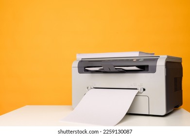 Front view of a light printer and a blank A4 paper on a white table on a yellow background, mockup.Office equipment, close-up.Copy space.Multifunction device. Multifunction printer.