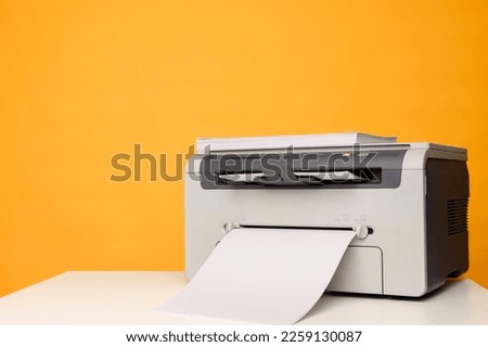 Front view of a light printer and a blank A4 paper on a white table on a yellow background, mockup.Office equipment, close-up.Copy space.Multifunction device. Multifunction printer.