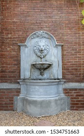 front view of lion head sculpture water fountain with small water stream from mouth on brick wall.