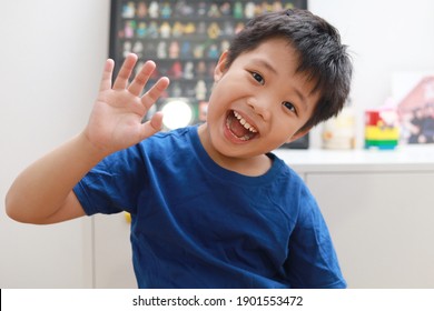 Front view of a little Asian boy waving hand and talking to the camera video calling video conference with his friend and family during the pandemic lockdown.