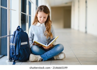 Front view of little beautiful school girl among corridor at school, holding notes at hands. Funny and happy girl smiling at camera, resting after lessons on primary school. - Powered by Shutterstock