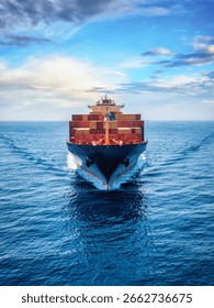 Front view of a loaded container cargo vessel traveling over calm ocean with speed