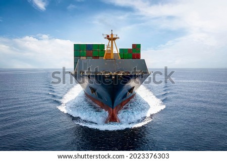 Front view of a loaded container cargo vessel traveling with speed over blue ocean