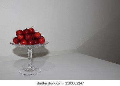 Front view of luscious red plums on a glass serving platter on a white table and in front of a white background