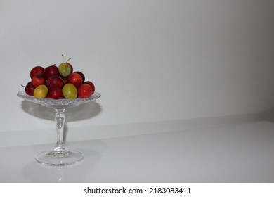 Front view of luscious red plums and green plums on a glass serving platter on a white table and in front of a white background - Shutterstock ID 2183083411