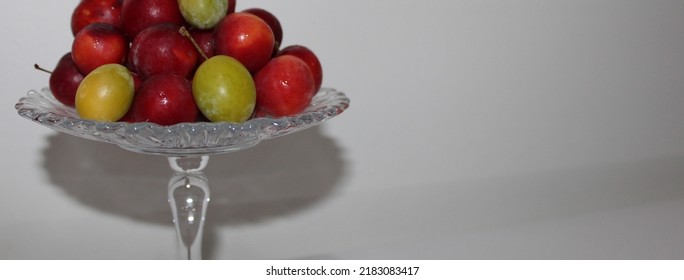 Front view of luscious red plums and green plums on a glass serving platter on a white table and in front of a white background - Shutterstock ID 2183083417