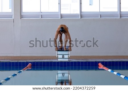 Front view of male Caucasian swimmer at swimming pool, jumping from starting blocks, plunging into water. Swimmers training hard for competition.