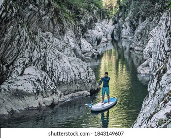 Front view of man floating on SUP on river water in rocky canyon with stone walls