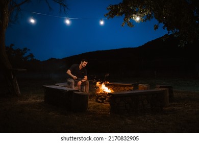 Front view of a man sitting next to a campfire at sunset, he is looking at the fire, a guitar next to him. The concept of tourism, camping, tourism.