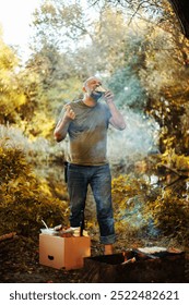 Front view of a man standing next to a campfire at autumn forest, he eat food prepared in the fire. The concept of tourism, camping, tourism.